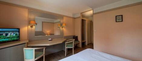 Habitación de hotel con cama, escritorio, silla, televisor y espejo.