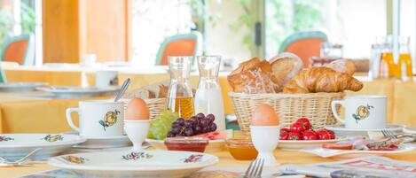 Desayuno con cruasanes, huevos, uvas y tomates sobre una mesa.