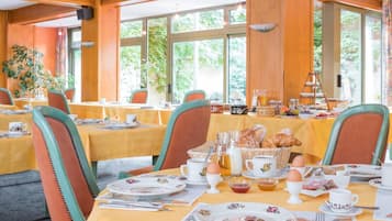 Un comedor con mesas dispuestas para el desayuno, mostrando pan, huevos y bebidas.