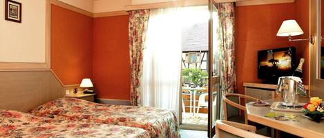Habitación de hotel con cama, escritorio con lámpara, televisión y vistas al exterior.
