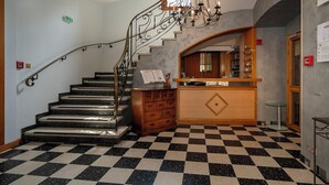 A hotel lobby with a checkered floor, a staircase with metal railings, a wooden reception desk, and a chandelier. - A la Vignette (Saint-Hippolyte)