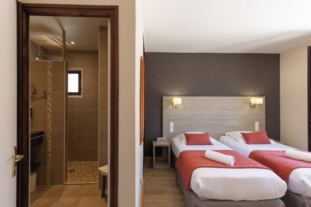 Ein Hotelzimmer mit zwei Betten, einer Duschkabine, einem kleinen Tisch und einem Nachttisch.