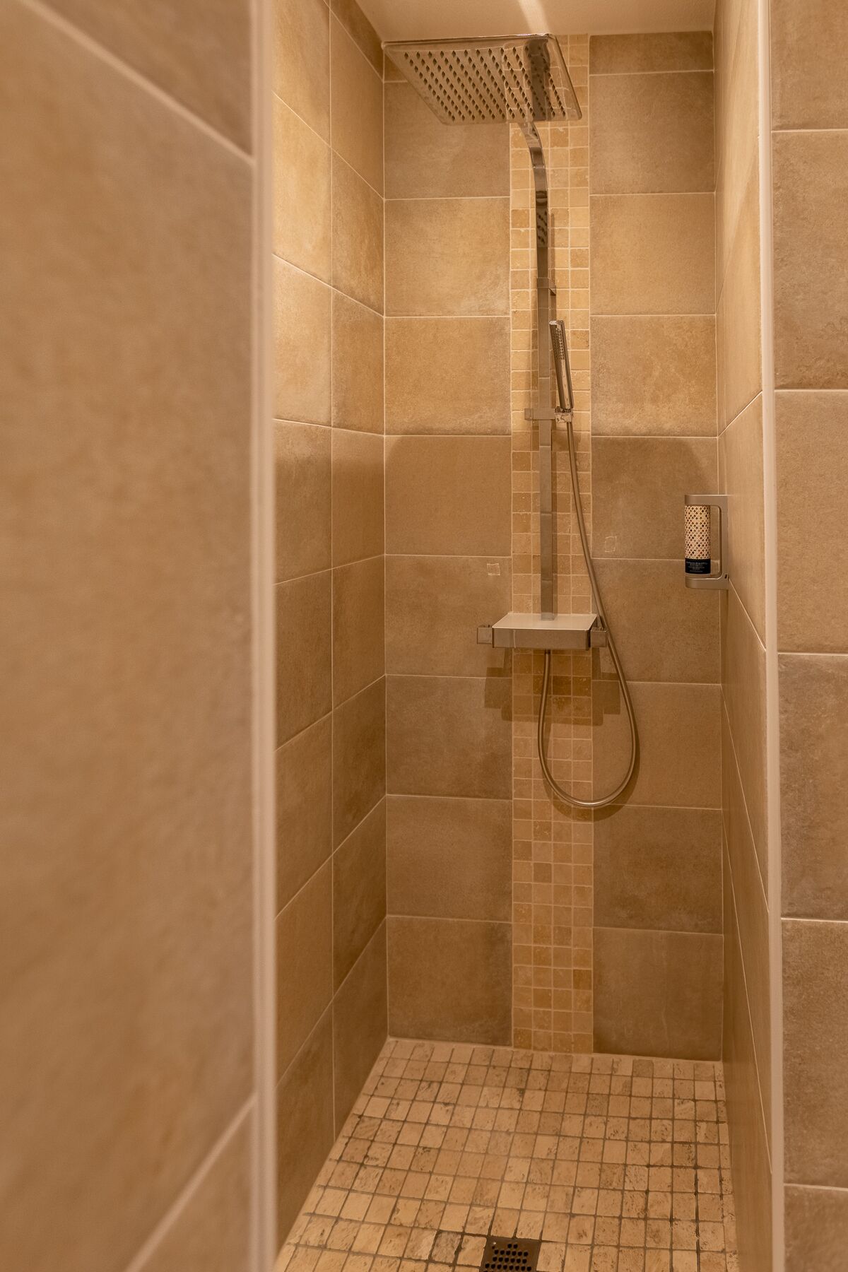 A walk-in shower with beige tiles, a handheld showerhead, and a wall-mounted control panel.