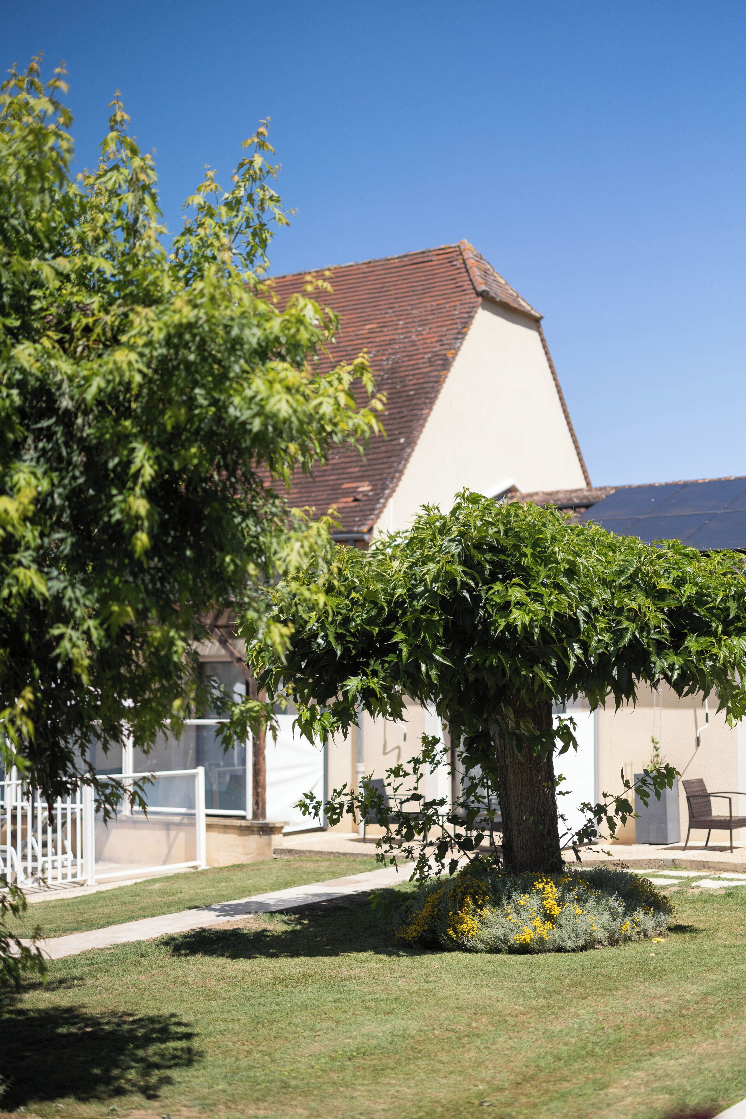 A house with a sloped roof, a tree in the front yard, and a white fence.