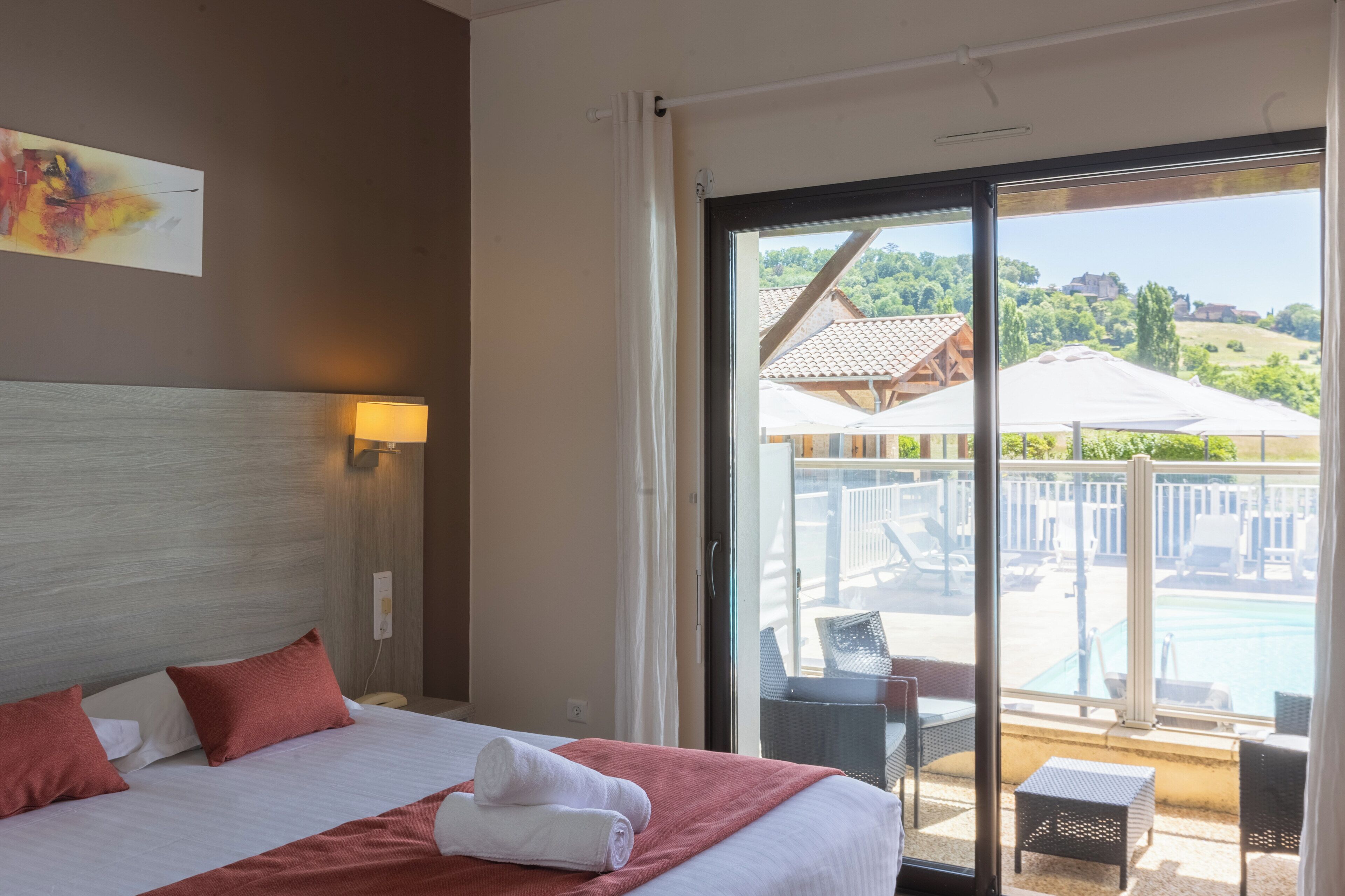 Een hotelkamer met een bed, uitzicht op een zwembad en buiten zitplaatsen, en een schilderij aan de muur.