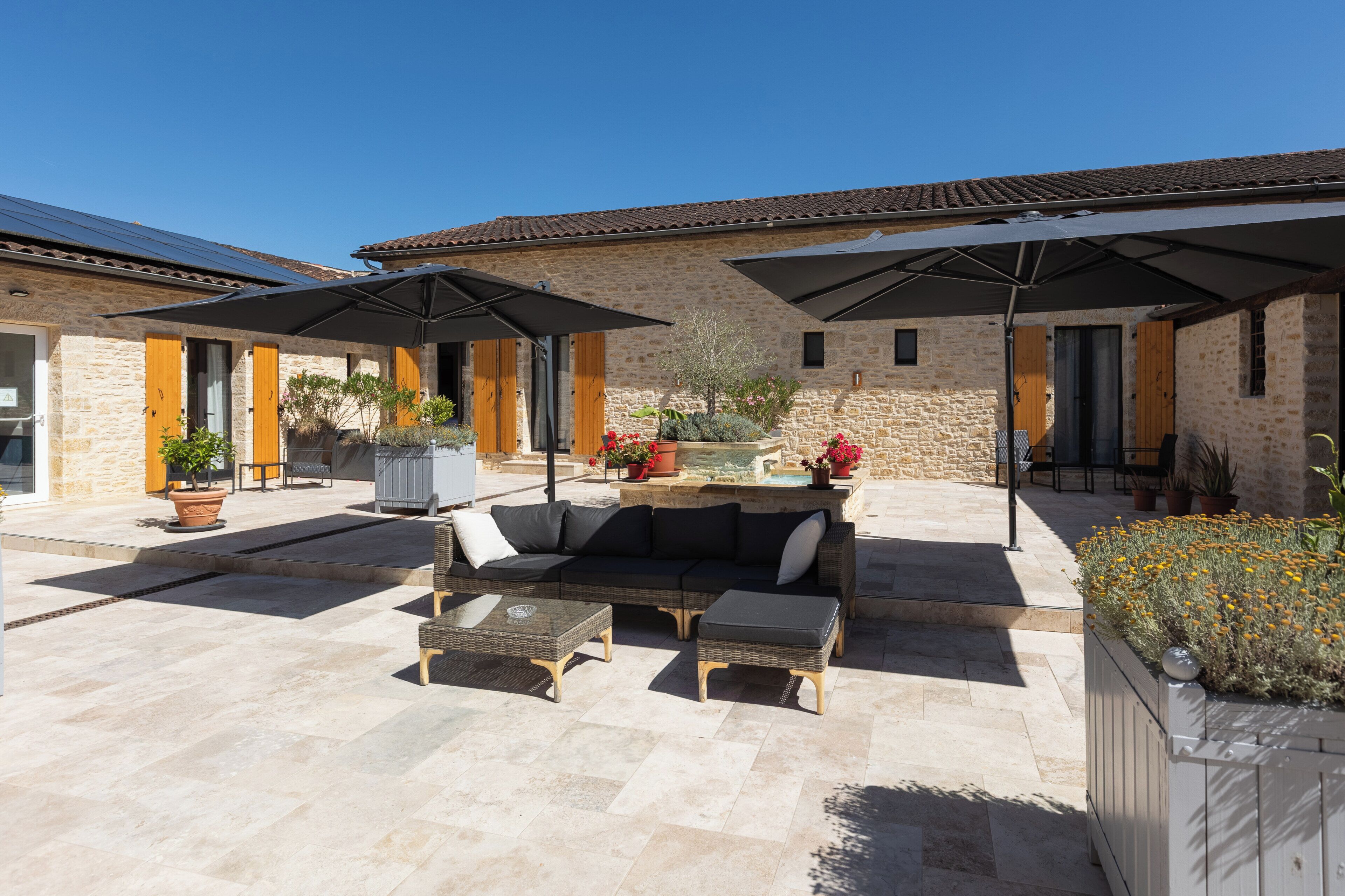 A stone building with a patio area featuring outdoor furniture, umbrellas, and potted plants.