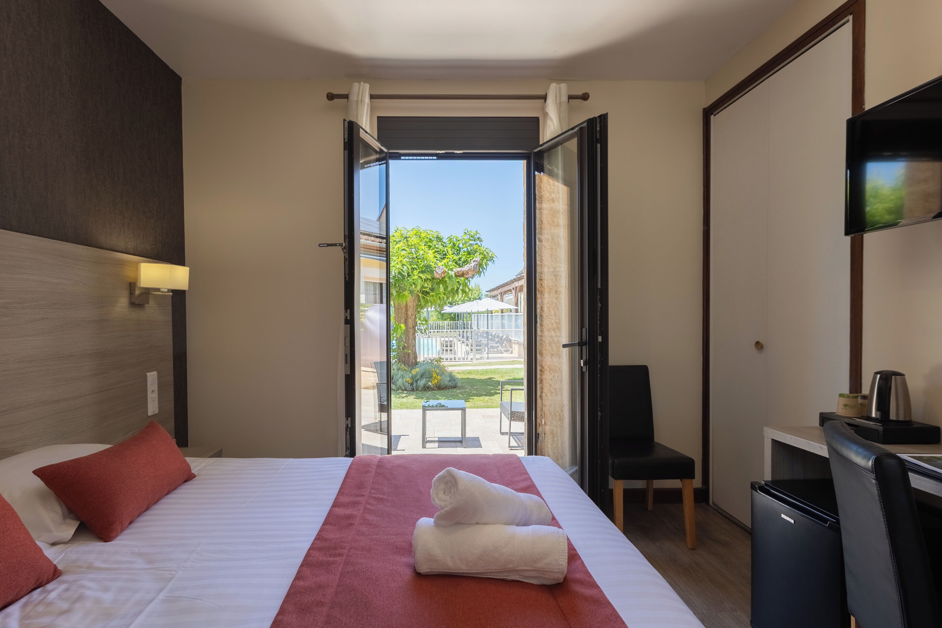 A hotel room with a bed, a desk, a chair, a TV, and a balcony with a view of the outside.