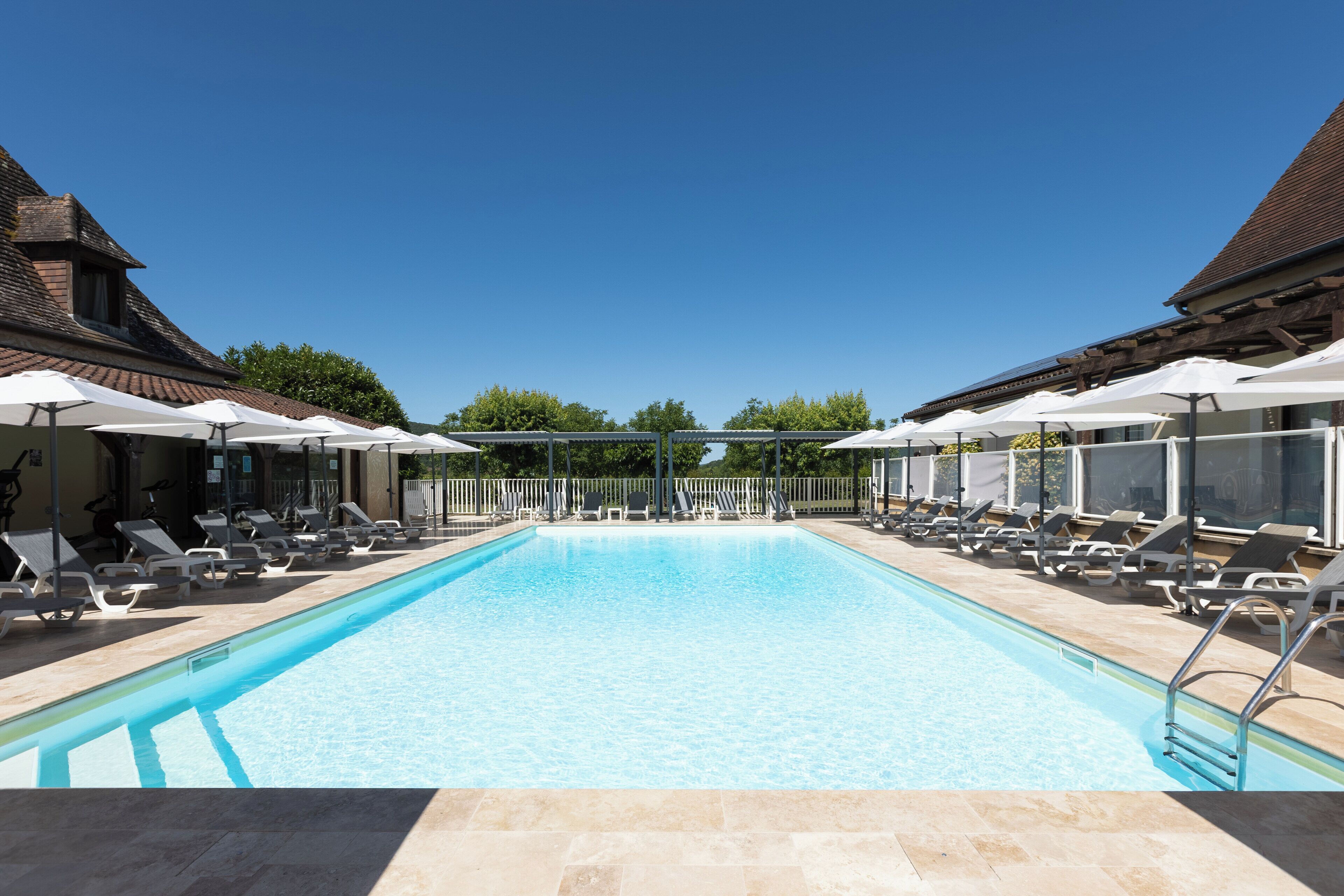 Ein rechteckiger Pool mit klarem, blauem Wasser, umgeben von Liegestühlen und Sonnenschirmen, mit einem Holzgebäude auf jeder Seite.