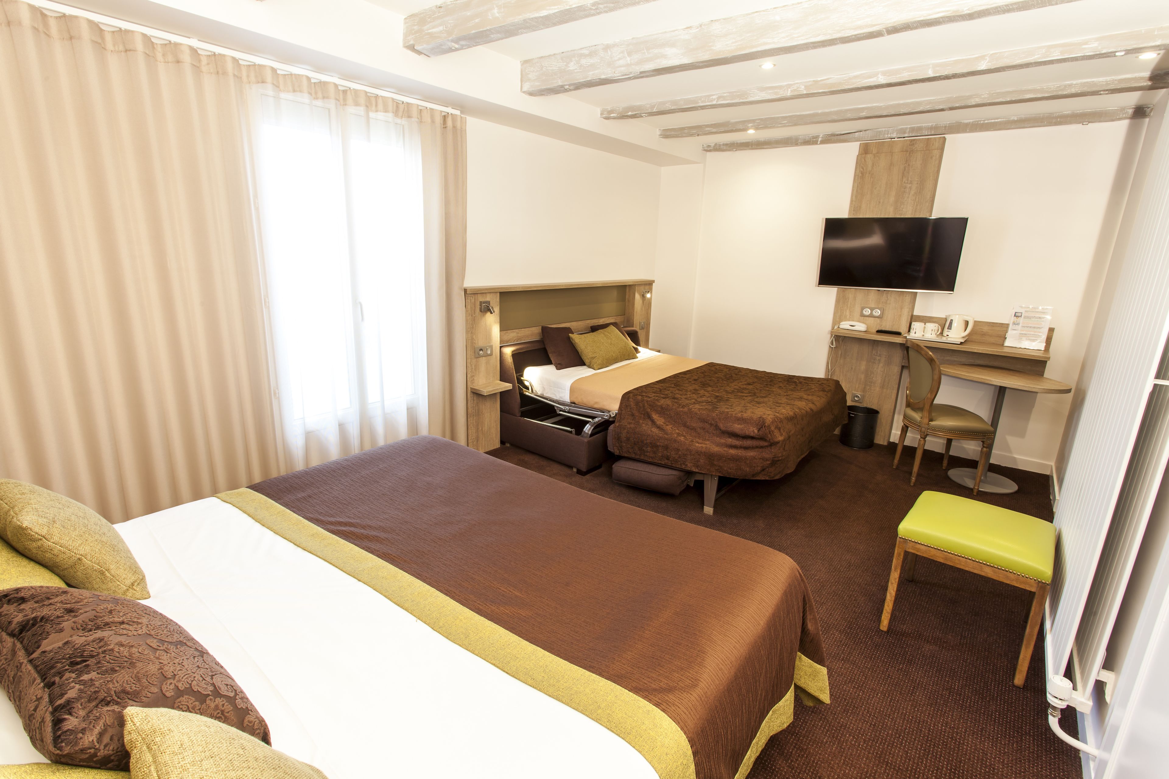 Quarto de hotel com uma cama grande, uma mesa com televisão de tela plana, uma cadeira e um banquinho pequeno.