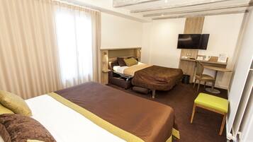 Quarto de hotel com uma cama grande, uma mesa com televisão de tela plana, uma cadeira e um banquinho pequeno.
