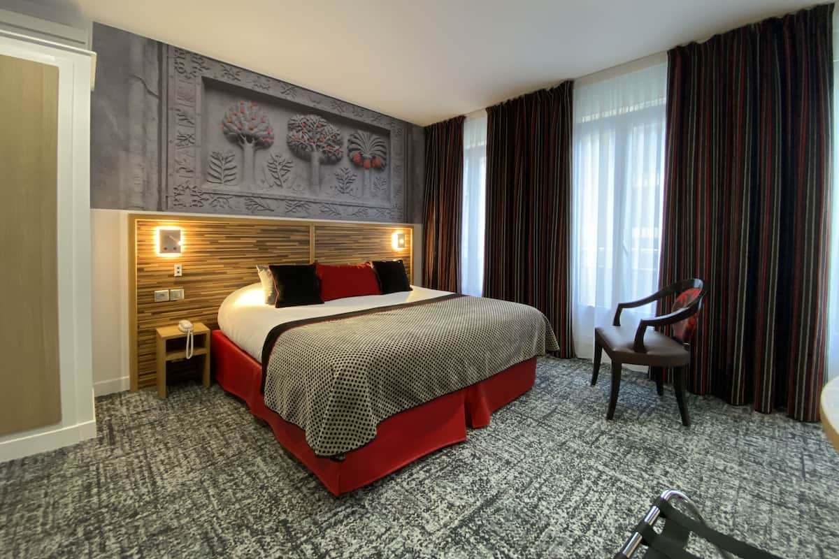 A hotel room with a large bed, a wooden headboard, a nightstand, a chair, and a wall mural.