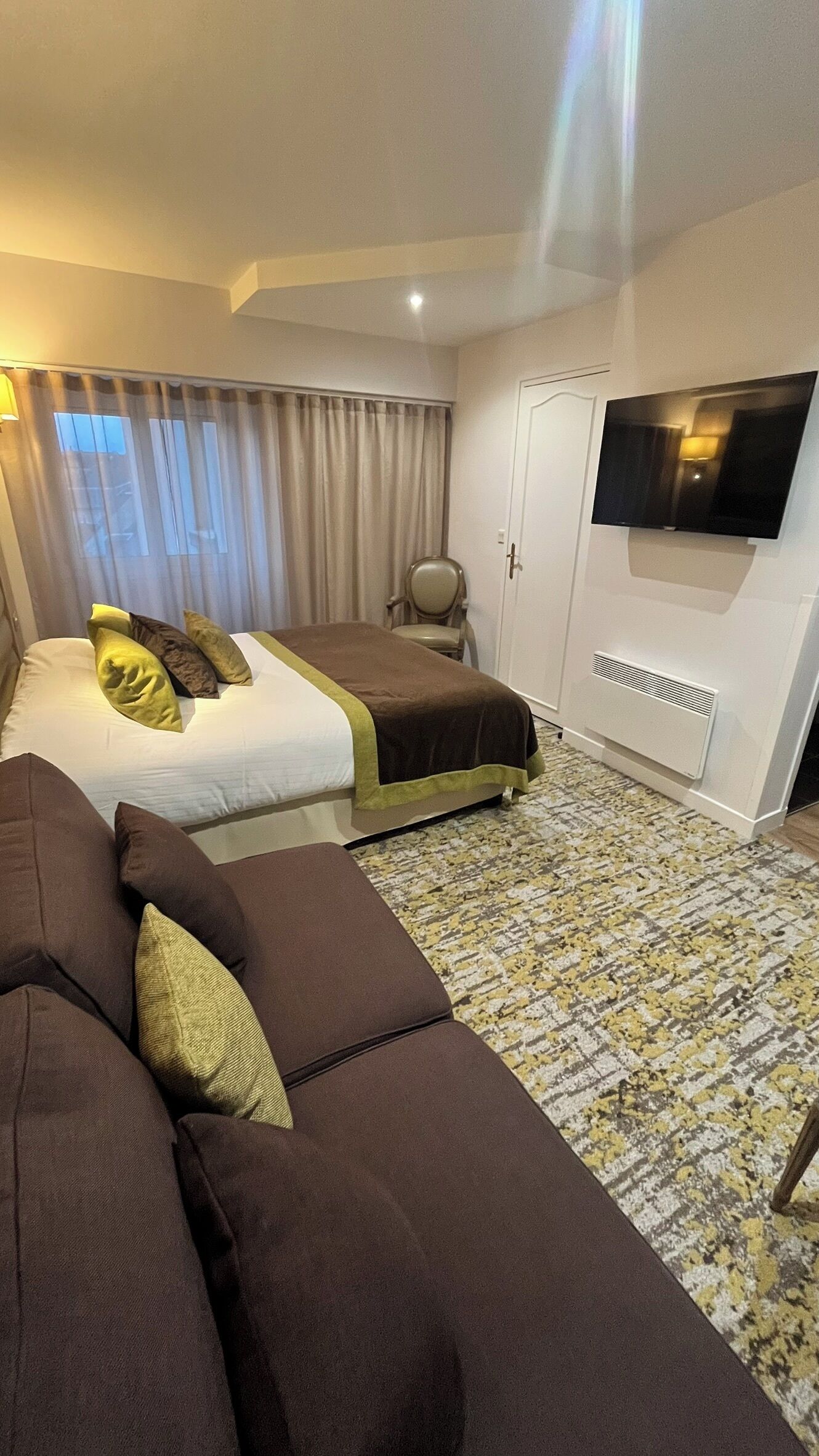 Una habitación de hotel con cama, sofá, televisor y puerta.