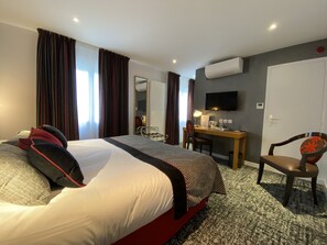 Habitación de hotel con una cama grande, un escritorio, una silla y un televisor en la pared.