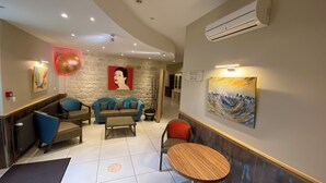 Un moderno vestíbulo de hotel con una pared de piedra, un conjunto de sofás azules, una mesa de centro de madera y un cuadro de un paisaje urbano.