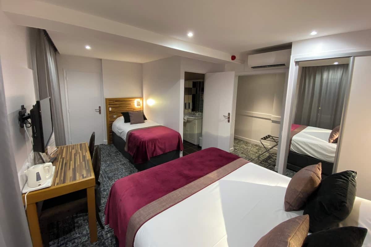 A hotel room with two beds, a desk with a coffee maker, a mirror, and a bathroom visible through an open door.