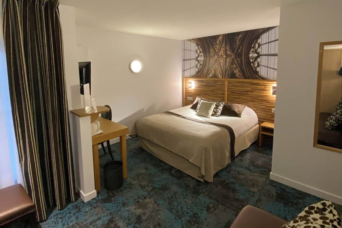 A hotel room with a bed, a desk, a chair, a small table, a round table, and a sofa.