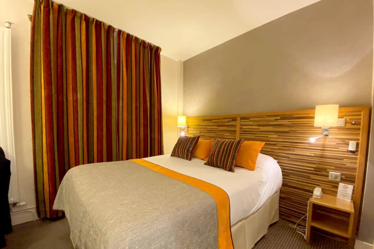 A hotel room with a large bed, striped curtains, a wooden headboard, bedside lamps, and a small bedside table.