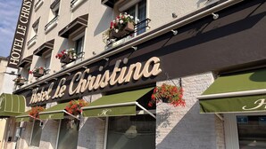 Hotel Le Christina con un letrero, jardineras de flores y toldos verdes.