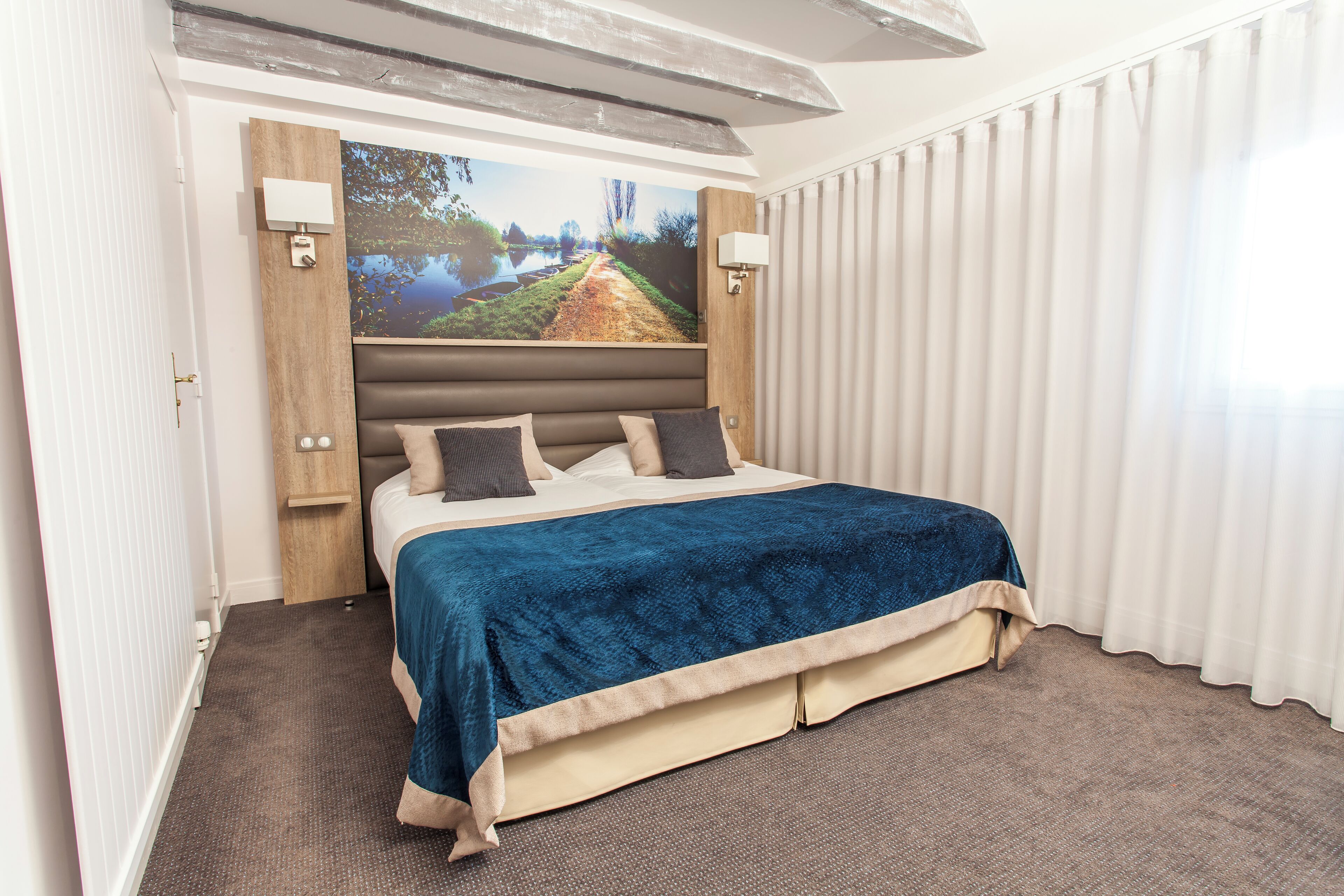 Una habitación de hotel moderna con una cama grande, un cabecero con televisor integrado y un amplio ventanal con cortinas.