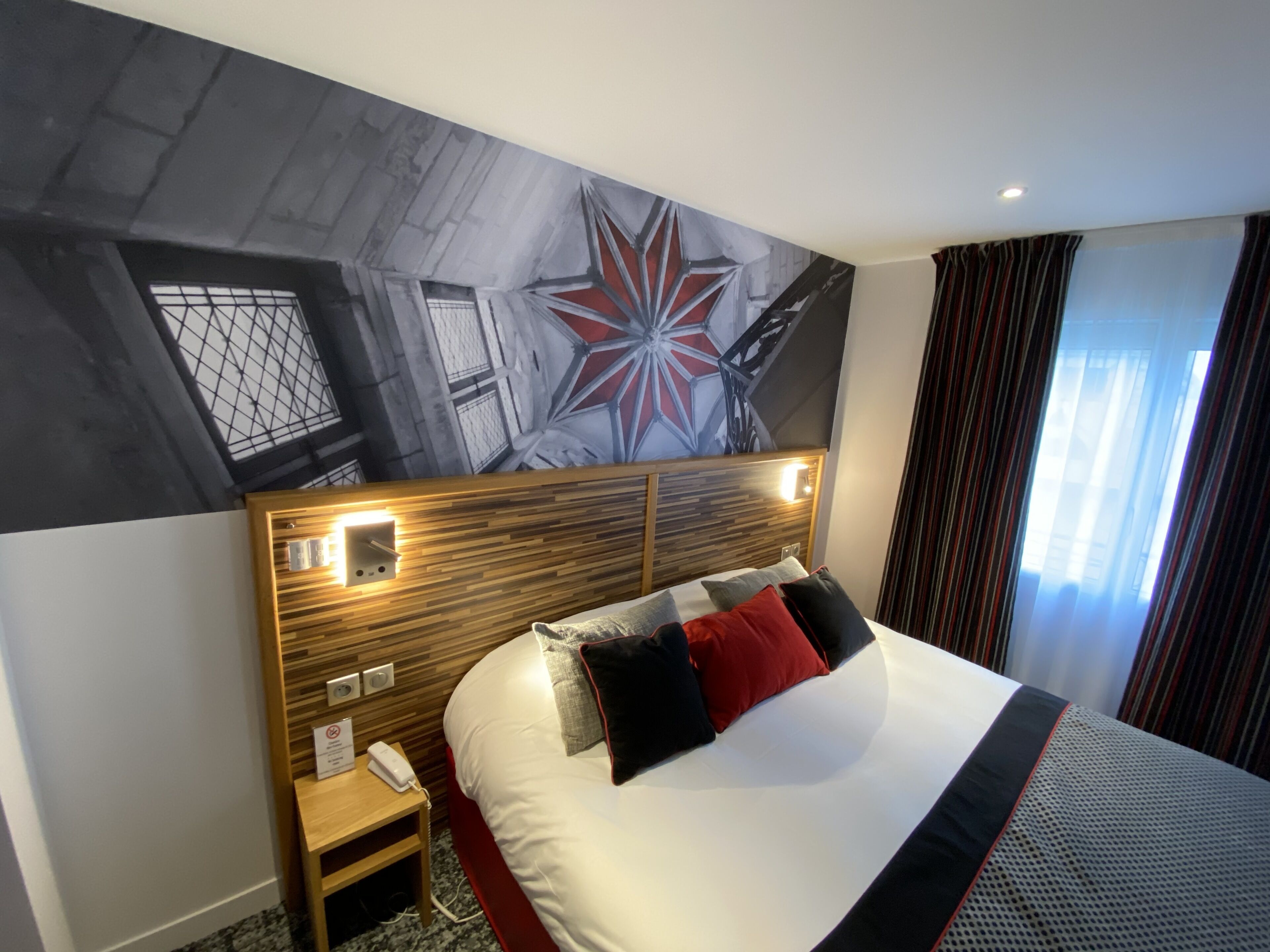 A hotel room with a large bed, a wooden headboard, a nightstand, a telephone, and a wall mural.
