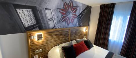 Una habitación de hotel con una cama grande, un cabecero de madera, una mesita de noche, un teléfono y un mural en la pared.