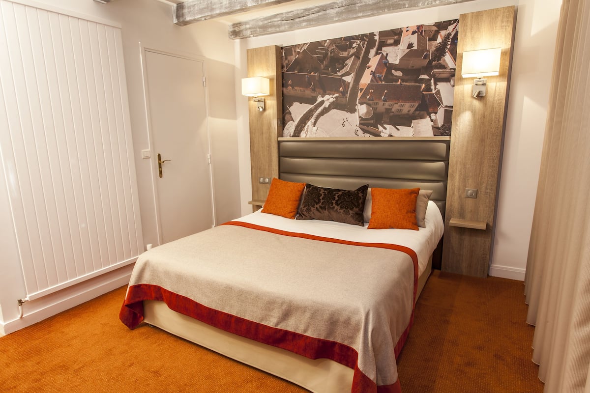 A hotel room with a bed, two wall-mounted lamps, and a cityscape artwork above the bed.