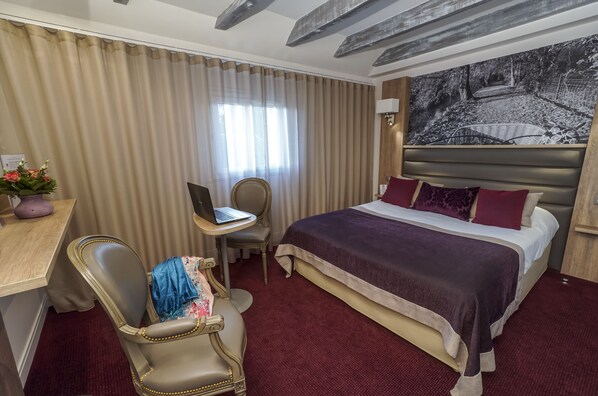 A hotel room with a bed, desk, chair, and a laptop.