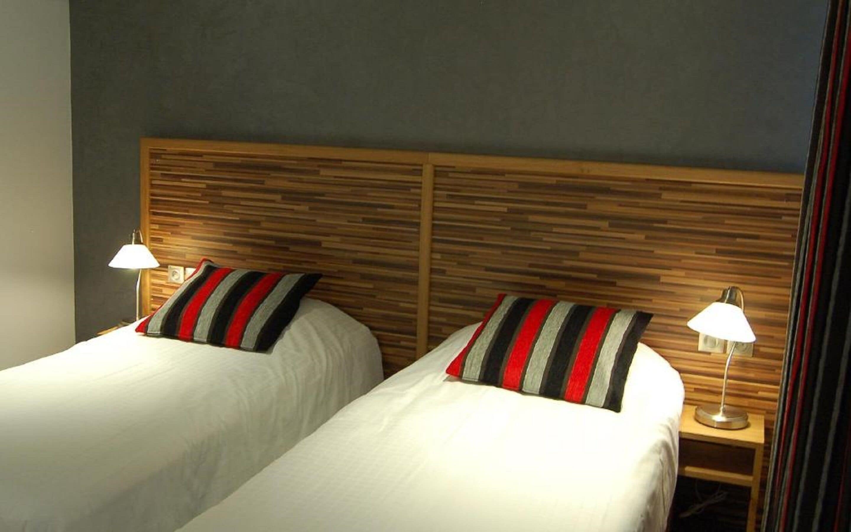Habitación de hotel con dos camas, cada una con un almohadón a rayas y una lámpara de noche.