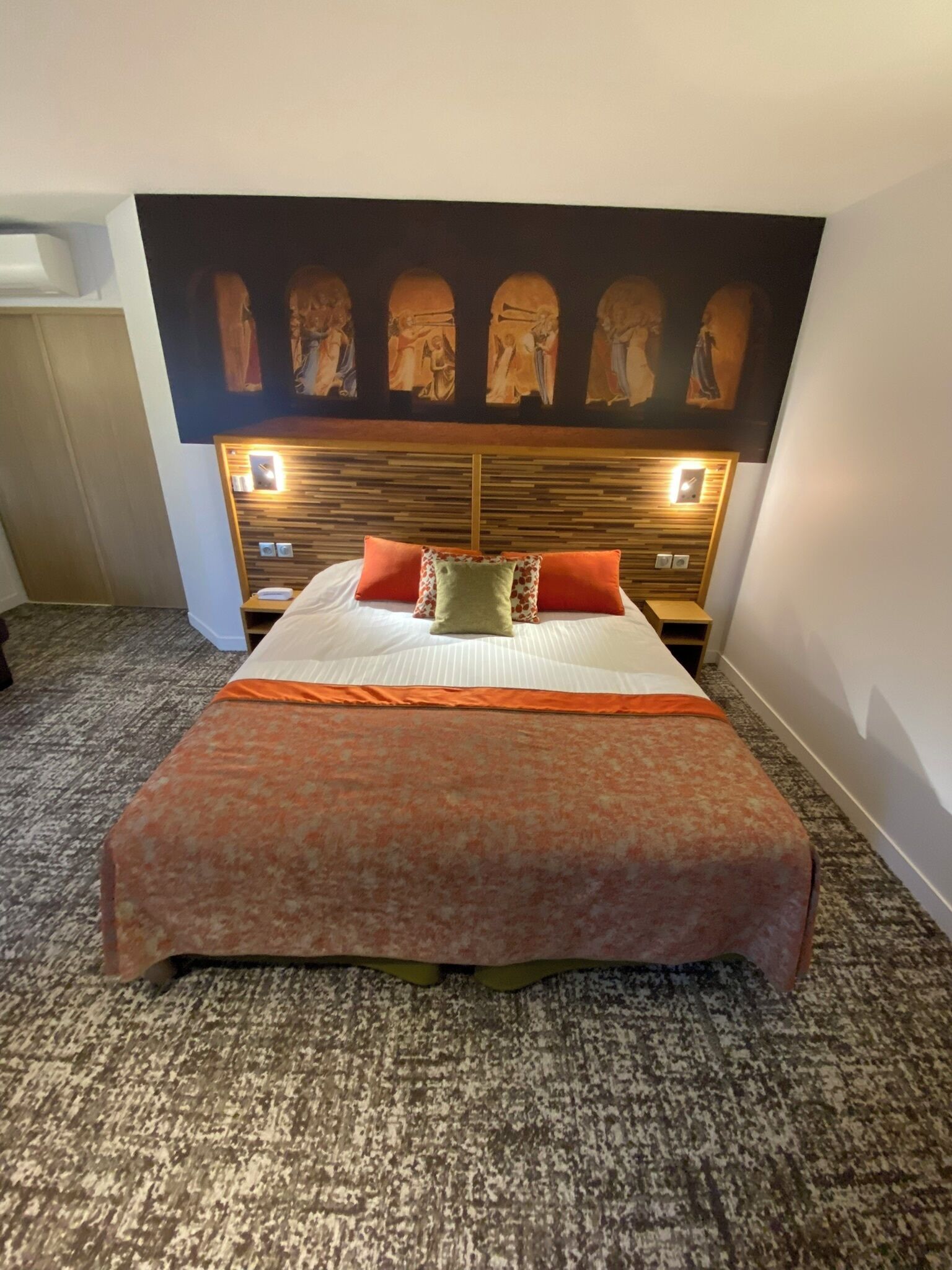 Una camera d'albergo con un letto grande, una testata decorata con opere d'arte e lampade ai lati del letto.