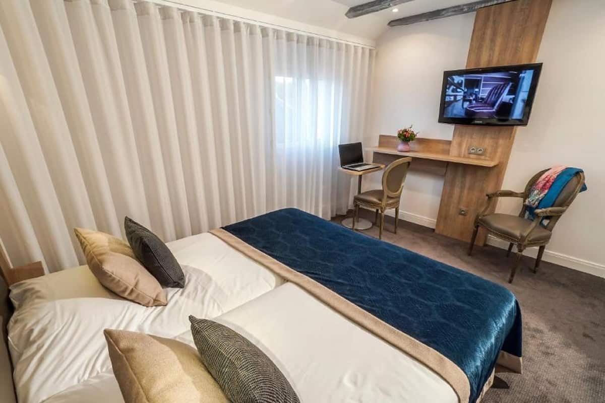 A hotel room with a bed, a desk, a chair, and a TV mounted on the wall.