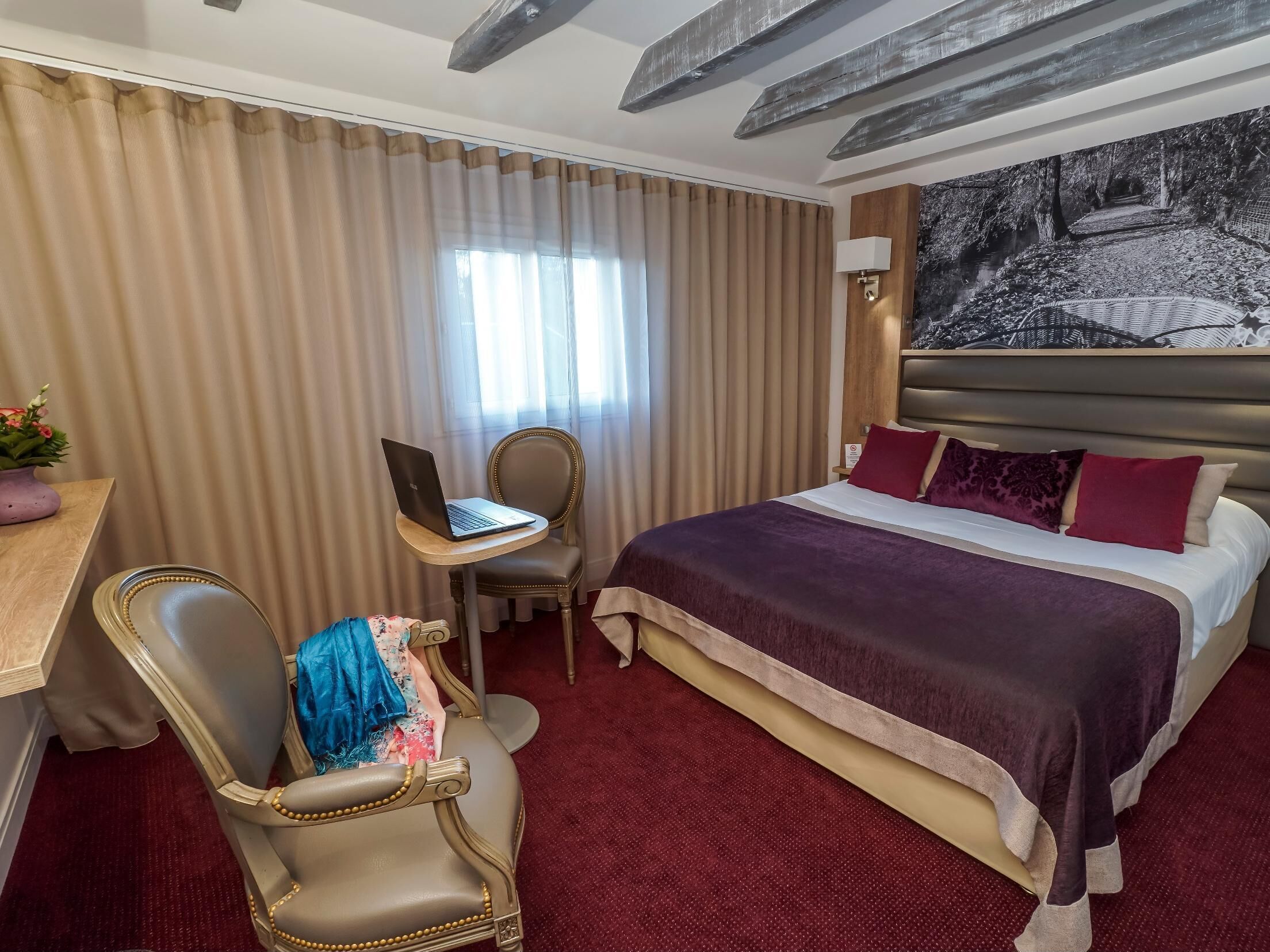 A hotel room with a large bed, a desk with a laptop, a chair, and a painting on the wall.