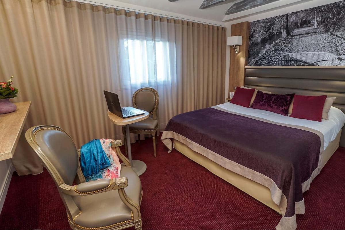A hotel room with a large bed, a desk with a laptop, a chair, and a painting on the wall.