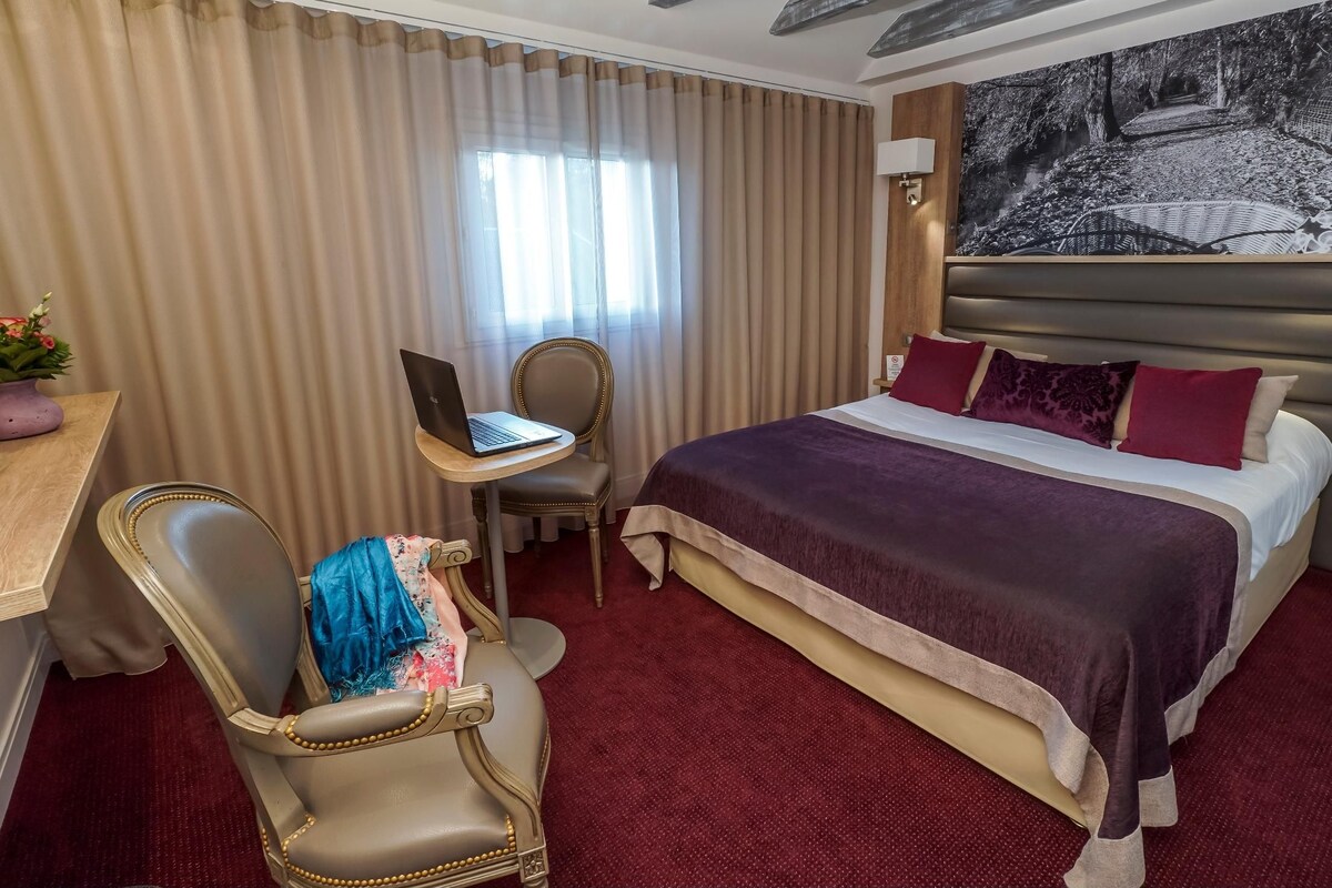 A hotel room with a large bed, a desk with a laptop, a chair, and a painting on the wall.