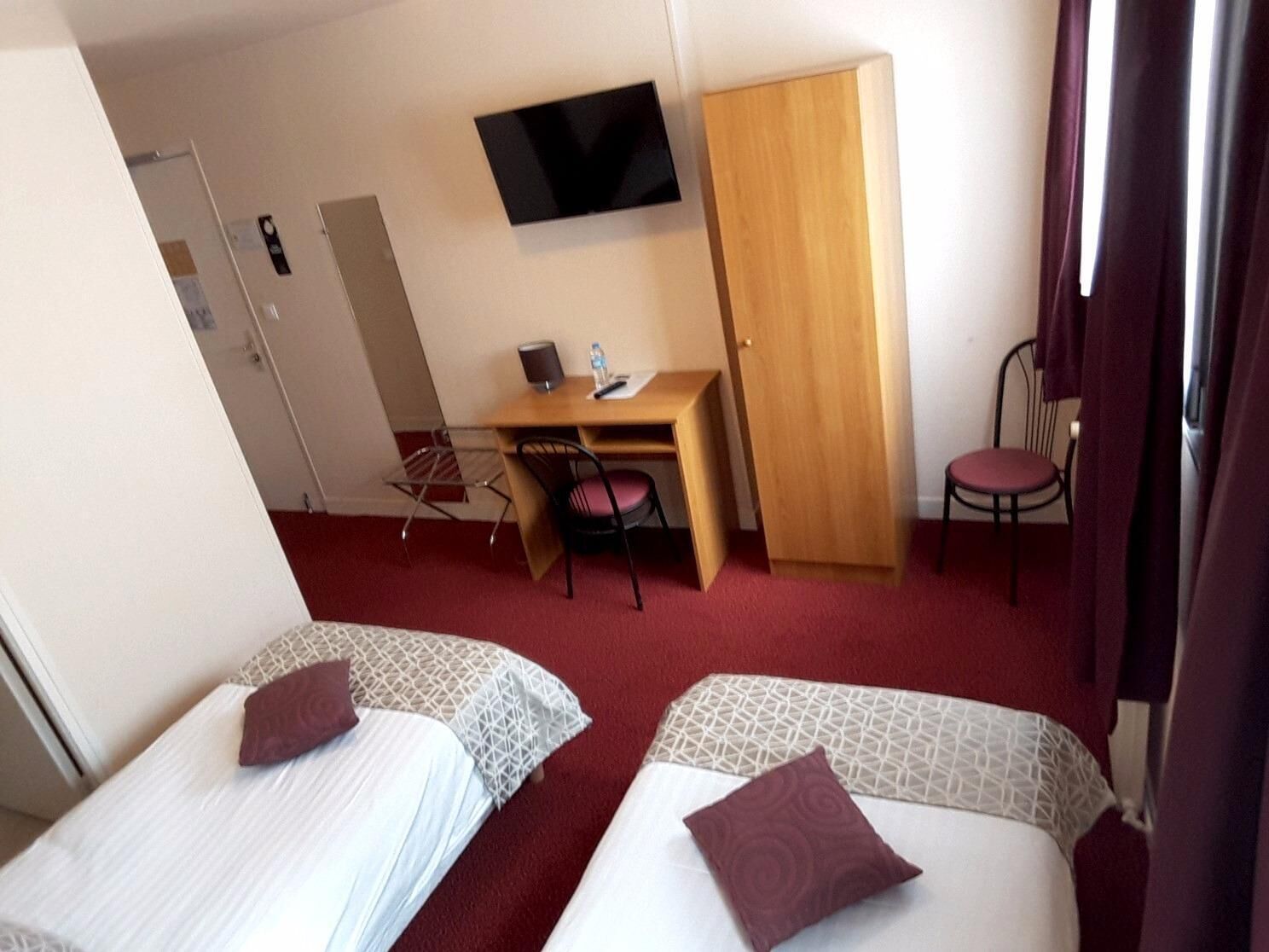Una habitación de hotel con dos camas, un escritorio con silla, televisión y armario.
