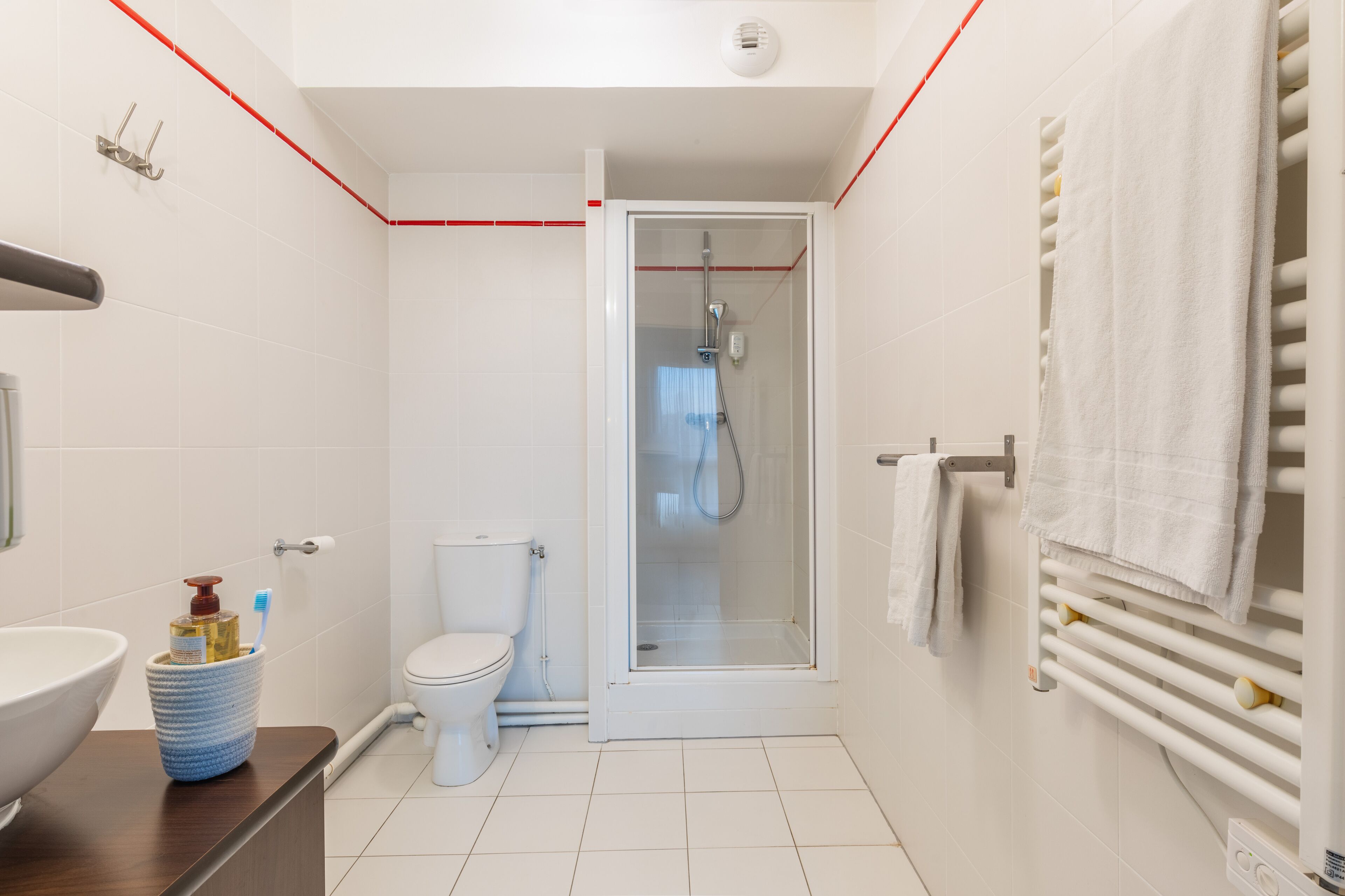Un baño moderno con ducha de vidrio, inodoro blanco y lavamanos con dispensador de jabón.