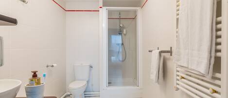 Un baño moderno con ducha de vidrio, inodoro blanco y lavamanos con dispensador de jabón.
