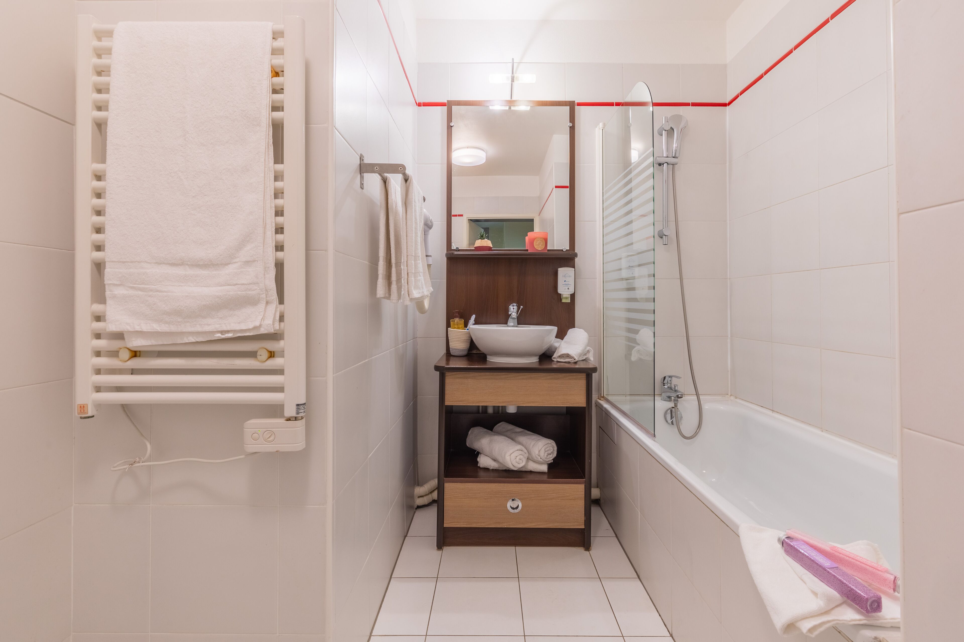 A bathroom with a white bathtub, a towel rack, a vanity with a sink, and a mirror.