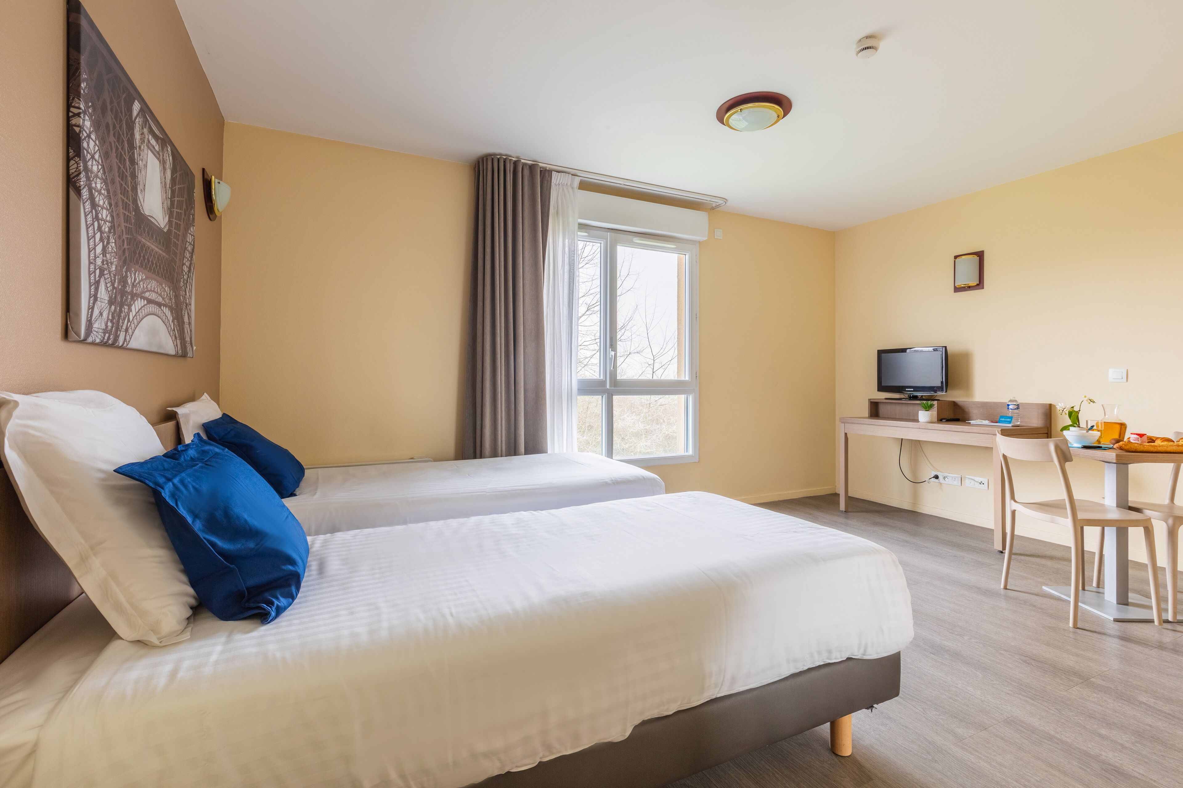 A hotel room with two beds, a desk, a chair, a television, and a window with curtains.
