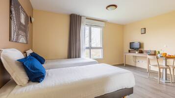 A hotel room with two beds, a desk, a chair, a television, and a window with curtains.