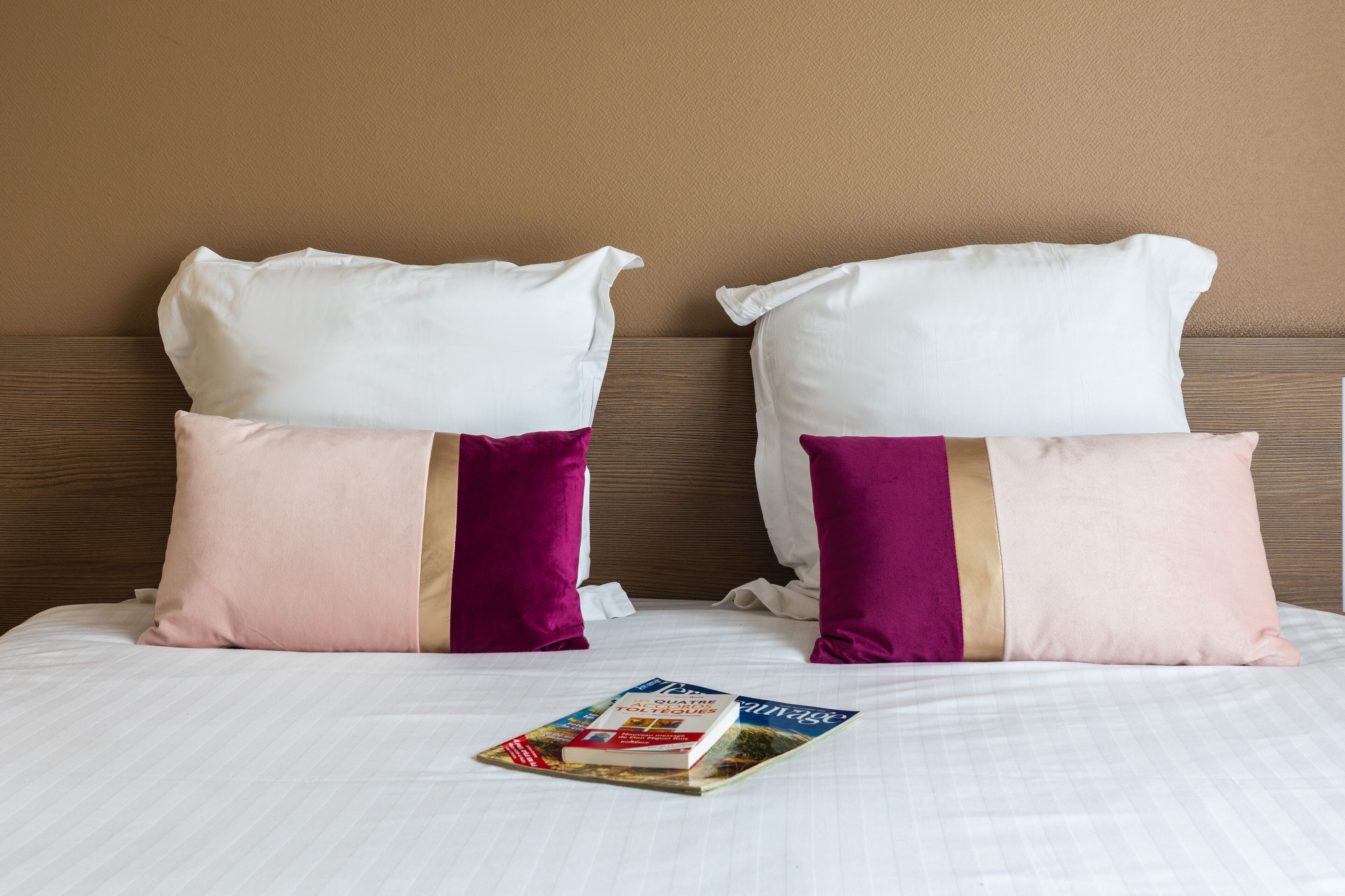 A hotel room with a bed, two pillows, and a magazine on the bed.