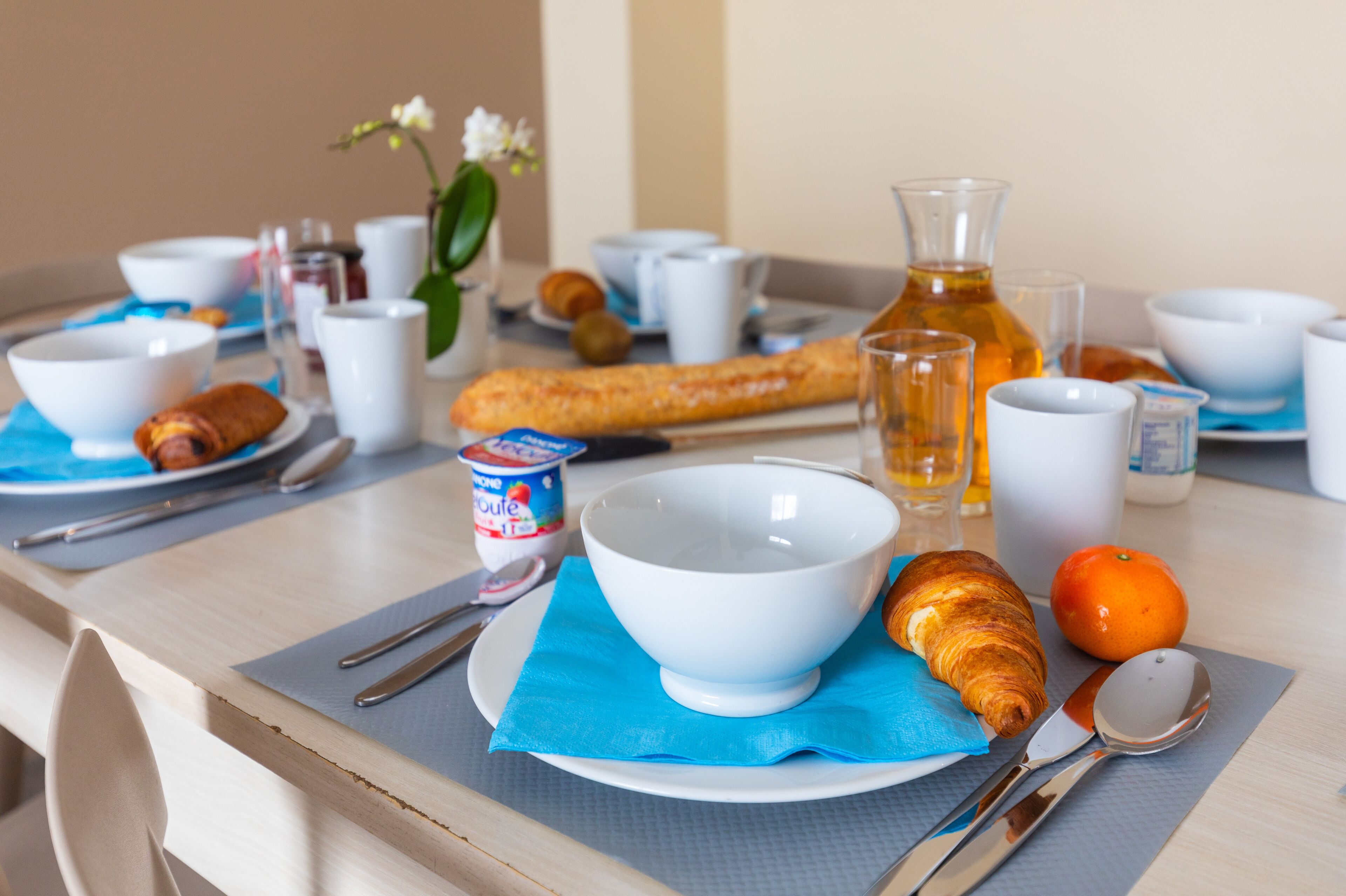 Une table de petit-déjeuner avec un croissant, une orange et une bouteille de jus.