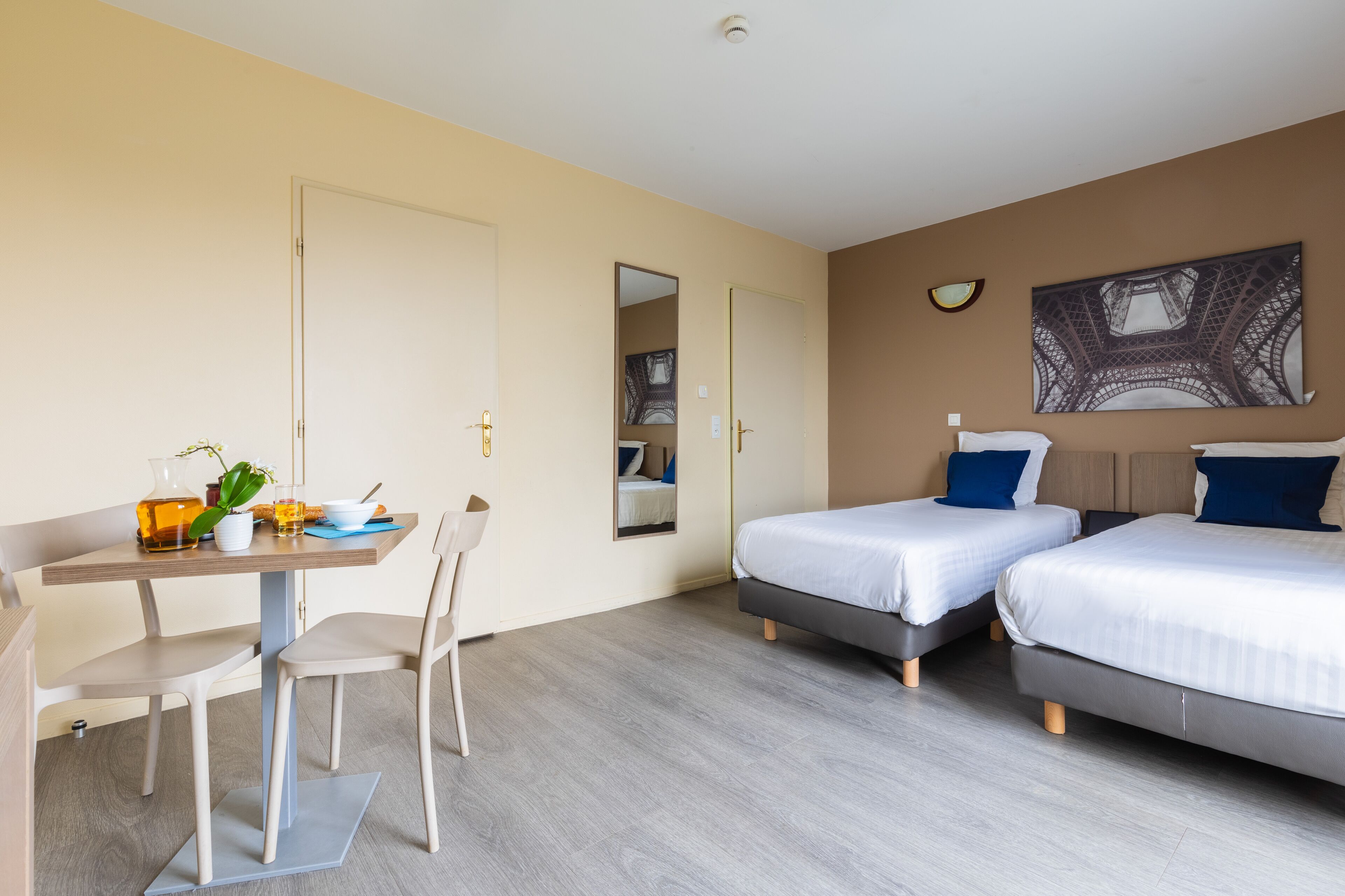 Une chambre d’hôtel avec deux lits, une table à manger avec des chaises, un petit coin cuisine et une grande fenêtre.