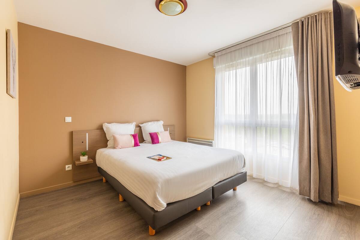 A neatly arranged bedroom with a bed, bedside table, and a window with curtains.