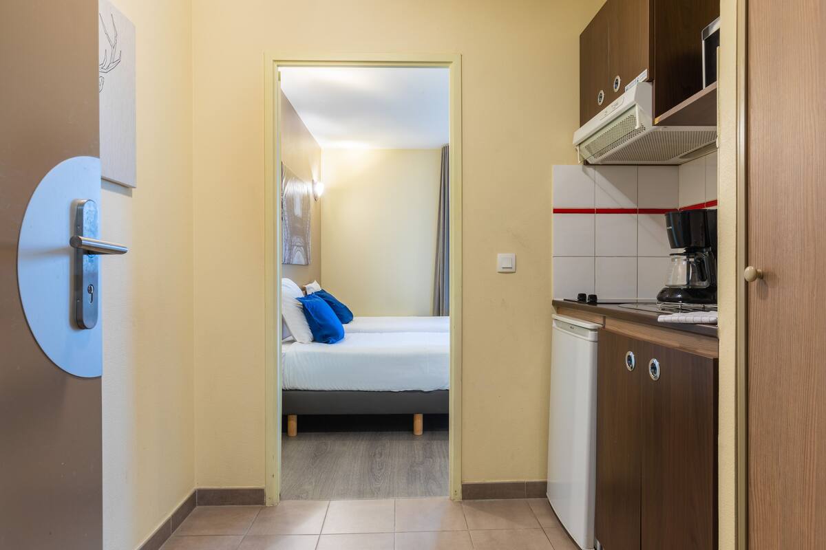 A narrow hallway leading to a bedroom with a bed, a small kitchenette, and a bathroom.