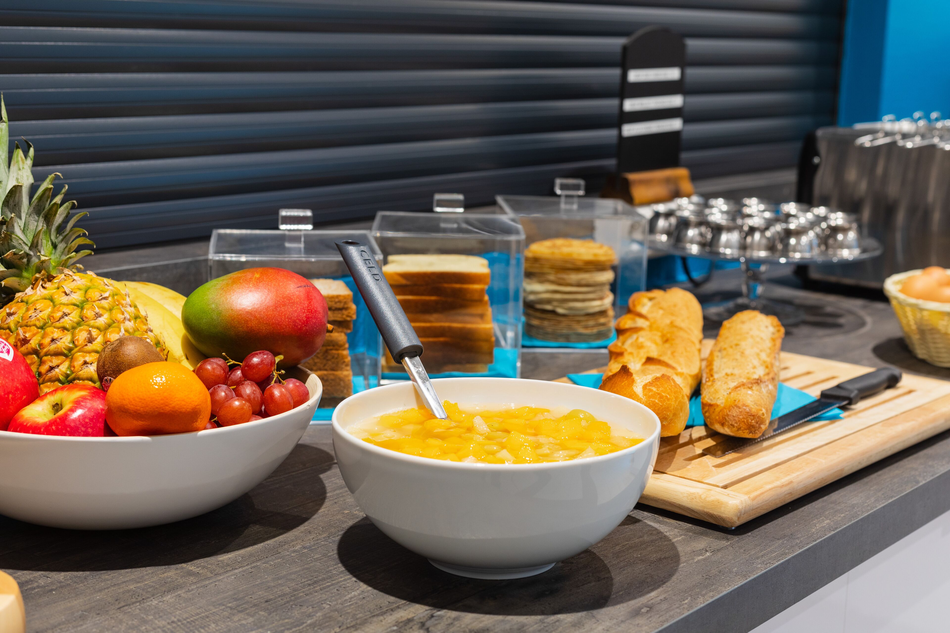 Un buffet de petit-déjeuner proposant une variété de fruits, de viennoiseries et une planche à découper avec un couteau.