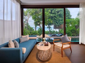 A modern living room with a large window, a blue sofa, a wooden chair, and a small round table. - Mercure Samui Chaweng Tana Hotel (Koh Samui)