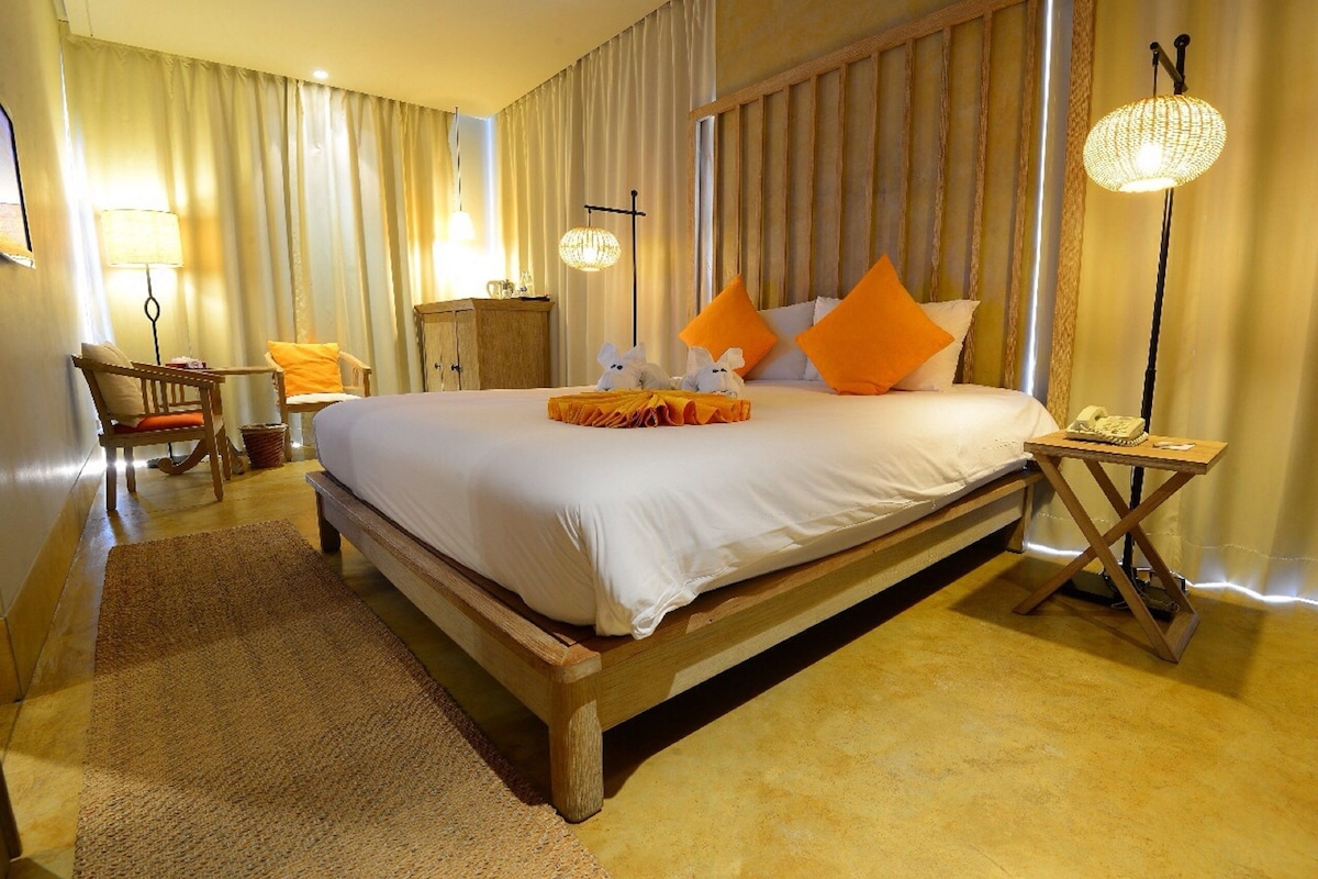 A hotel room with a large bed, wooden headboard, and a nightstand with a lamp.