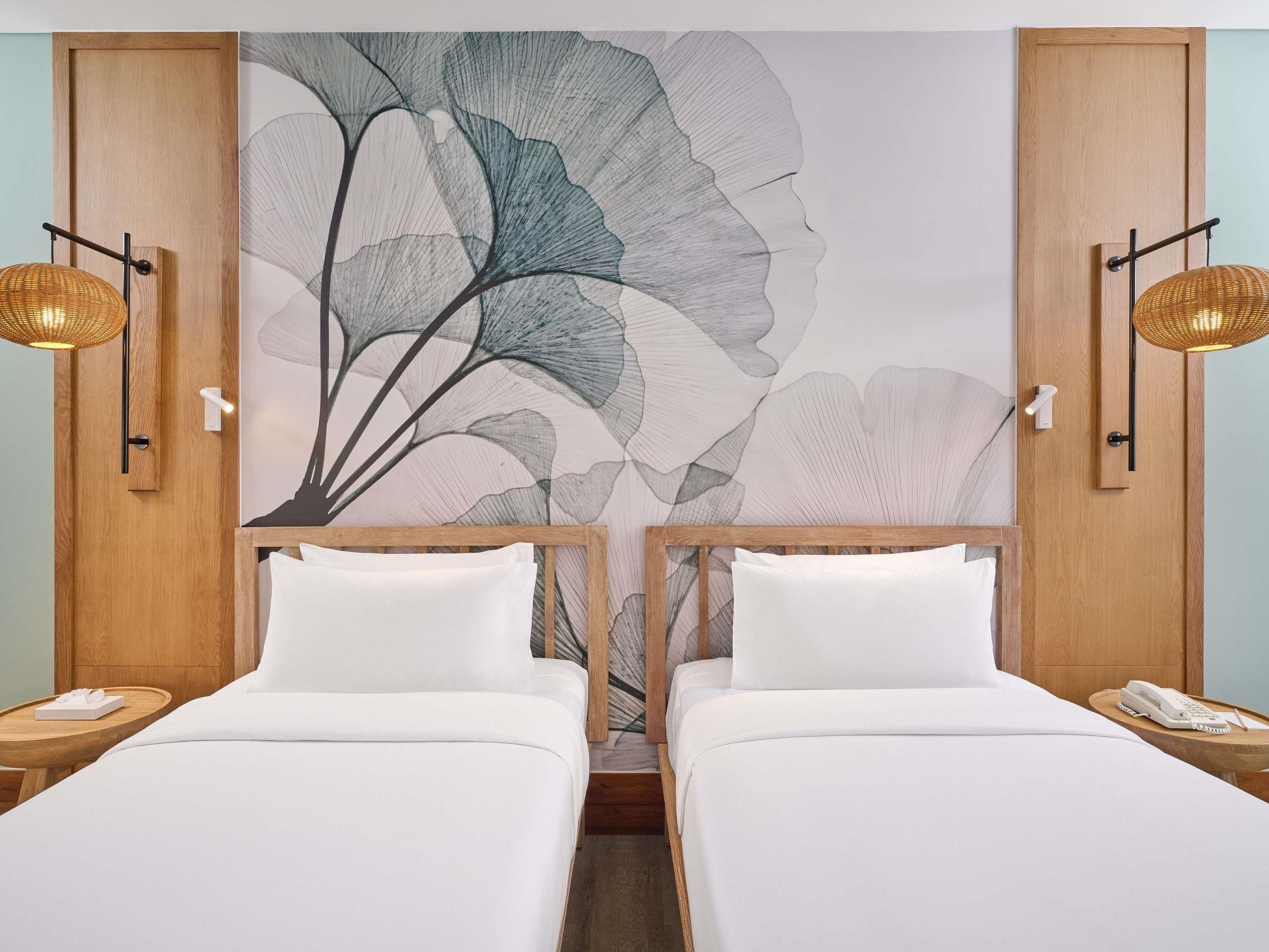 A hotel room with two beds, a large floral wall mural, and two bedside lamps.