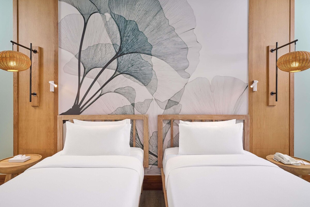 Habitación de hotel con dos camas, un gran mural floral en la pared y dos lámparas de noche.