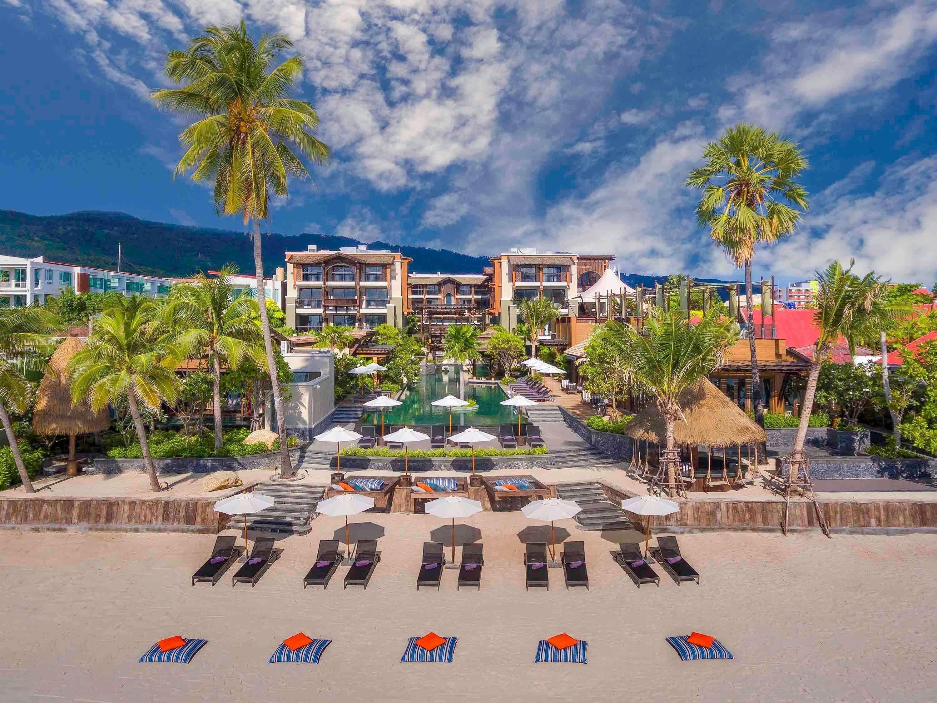 A resort with a pool, sun loungers, and palm trees.